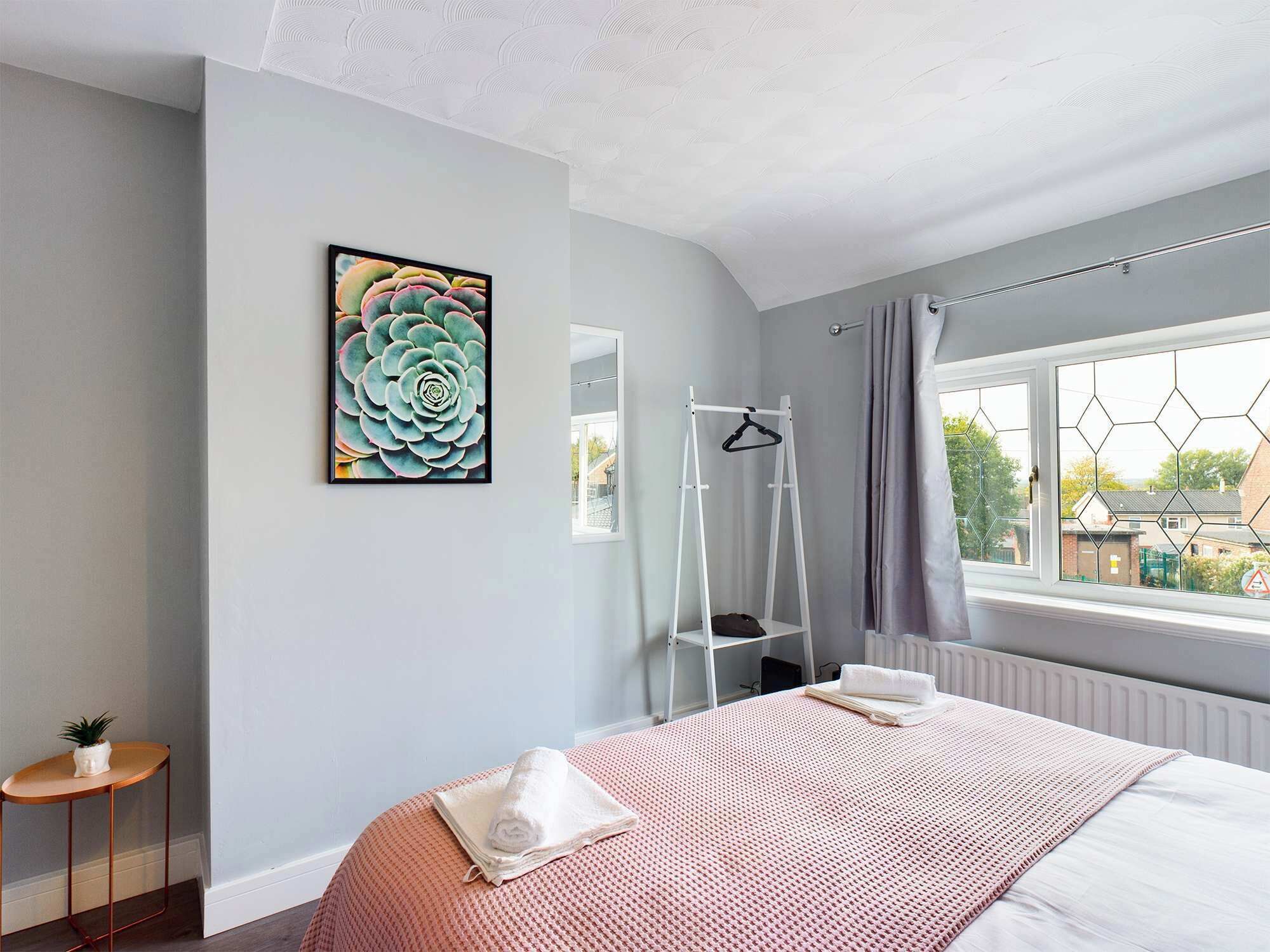 Une chambre à coucher avec un lit, une fenêtre avec des rideaux, un radiateur et une œuvre d’art accrochée au mur.