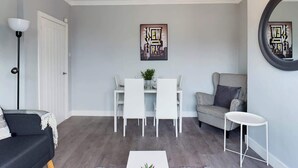 A living room with a dining area, a black sofa, a patterned armchair, a white coffee table, and a chandelier. - Comfortable 3 Bedroom House Sleeps 5 With WiFi (Hindley)