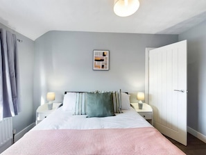 A bedroom with a bed, two bedside tables, a nightstand, a door, and a wall-mounted picture.