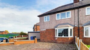 A residential property with a paved patio, a brick house, and a fenced garden area. - Comfortable 3 Bedroom House Sleeps 5 With WiFi (Hindley)