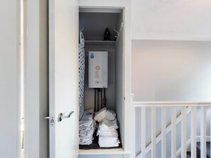 Un couloir étroit avec un radiateur blanc, une porte dotée d’une poignée et une rambarde blanche sur le côté droit.