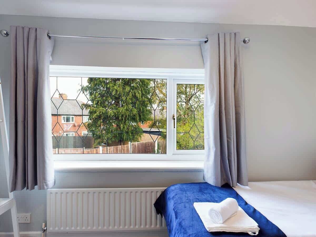 A bedroom with a bed, a window with curtains, and a view of the outside.