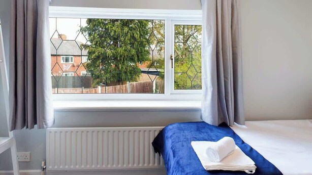 A bedroom with a bed, a window with curtains, and a view of the outside. - Comfortable 3 Bedroom House Sleeps 5 With WiFi (Hindley)