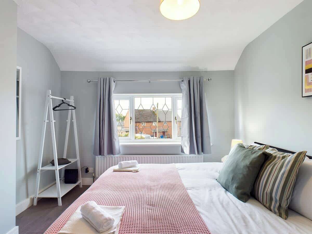 A bedroom with a bed, a window with curtains, a radiator, and a white shelf unit.