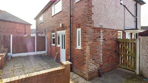A residential brick house with a front door, a small front yard, and a wooden gate. - Comfortable 3 Bedroom House Sleeps 5 With WiFi (Hindley)