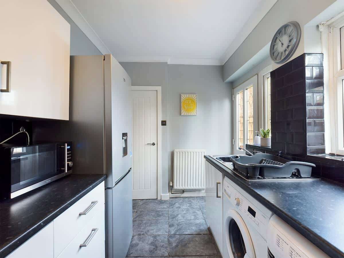 A compact kitchen with a microwave, refrigerator, sink, and a clock on the wall.