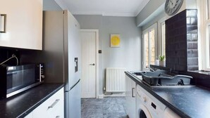 A compact kitchen with a microwave, refrigerator, sink, and a clock on the wall. - Comfortable 3 Bedroom House Sleeps 5 With WiFi (Hindley)
