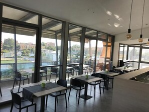 Uma área de refeições moderna em ambiente interno, com grandes janelas, mesas e cadeiras.