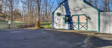 A rustic barn-style building with a green door and windows, surrounded by trees and a gravel driveway.