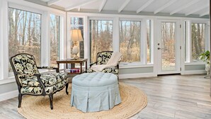 A conservatory with large windows, a wooden floor, and two upholstered chairs with a floral pattern. - Guilford Carriage House at Granite Lodge! (Guilford)