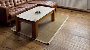 Un salon moderne avec un canapé d’angle en cuir marron, une table basse en bois et une grande fenêtre donnant sur une maison en briques.