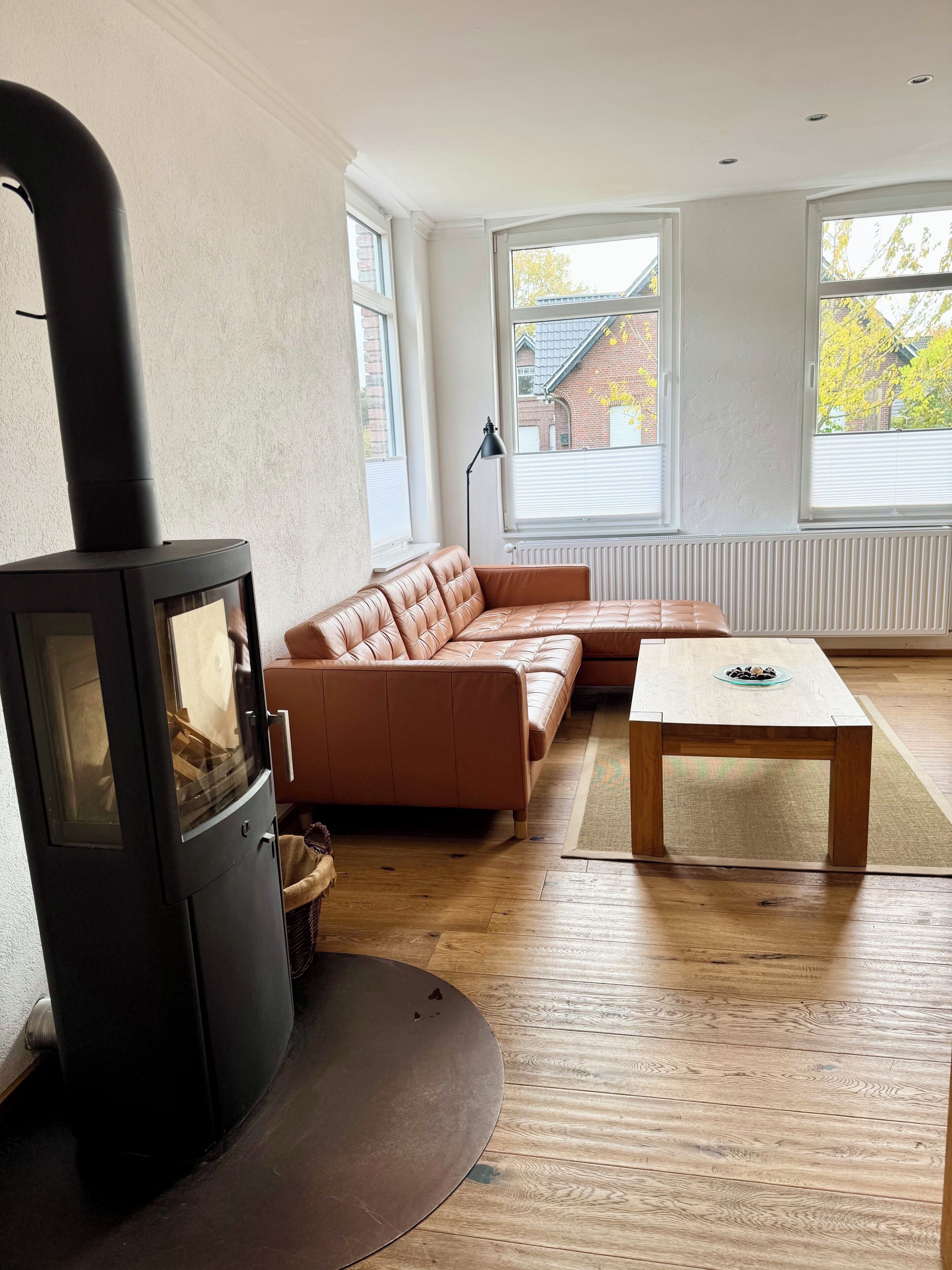 Un salon doté d’un poêle à bois, d’un canapé en cuir, d’une table basse en bois et de grandes fenêtres.