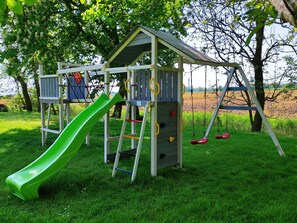 Eine Holzspielanlage mit Rutsche, Kletterwand und Schaukeln.