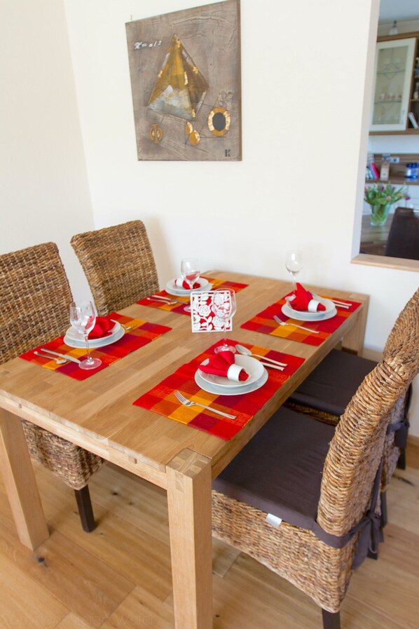 A dining table set with red napkins, white plates, and wine glasses, surrounded by wicker chairs.