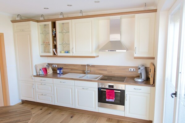 A modern kitchen with white cabinetry, a built-in oven, a coffee maker, and a sink. - Haus im Seewind I, 90sqm - Country house with large garden, near Friesenstrand (Butjadingen)