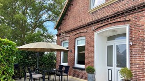 Une terrasse avec une table et des chaises, un grand parasol et des plantes en pot.