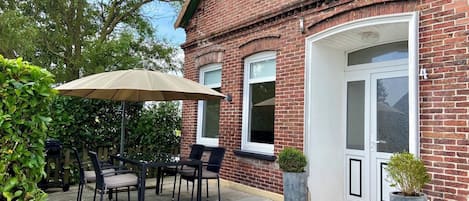Eine Terrasse mit Tisch, Stühlen, einem großen Sonnenschirm und Topfpflanzen.