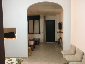 Um corredor que dá para uma sala de estar com sofá, televisão e uma porta.