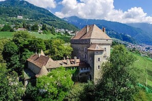 Un château doté d’une tour, entouré d’une végétation luxuriante et de montagnes.