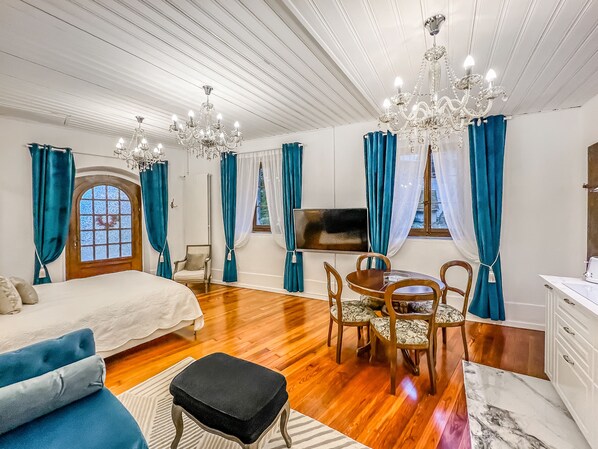 Une pièce spacieuse avec un grand lit, une table à manger avec des chaises, un lustre et un téléviseur.