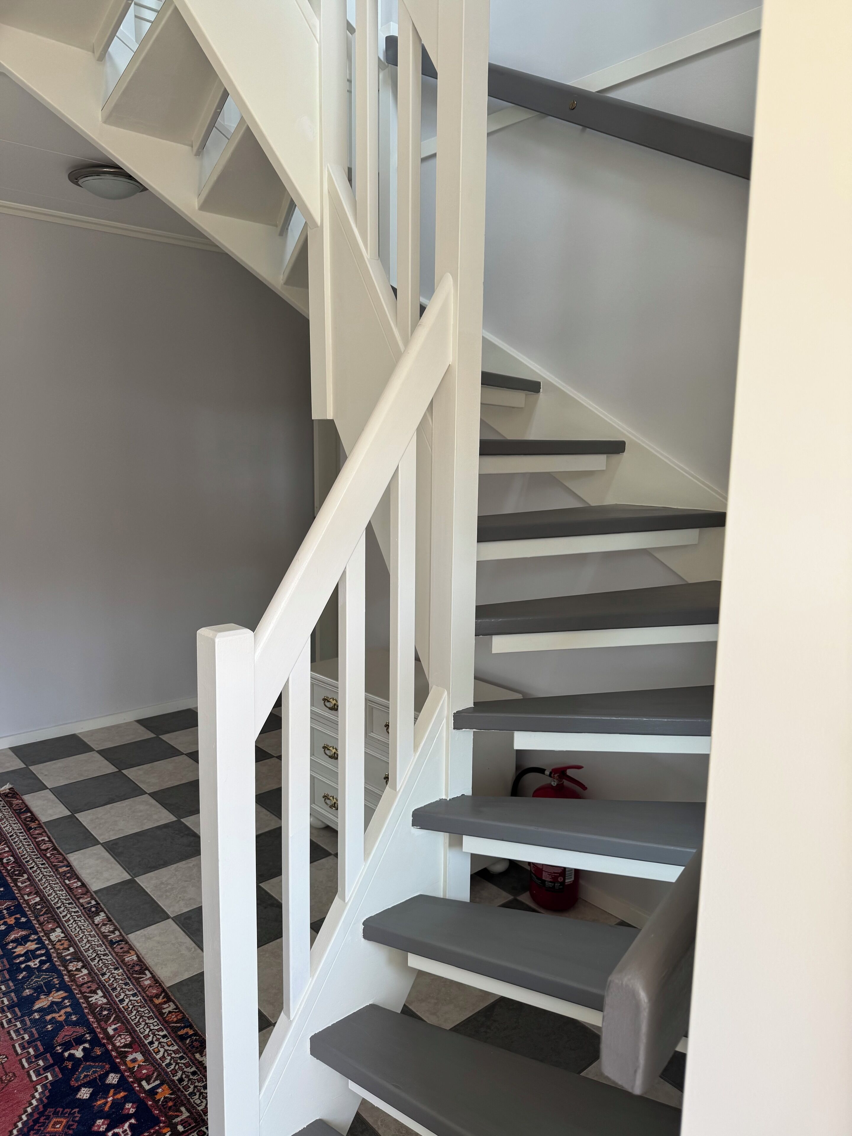 A staircase with white railings and grey steps, leading to a landing with a patterned rug.