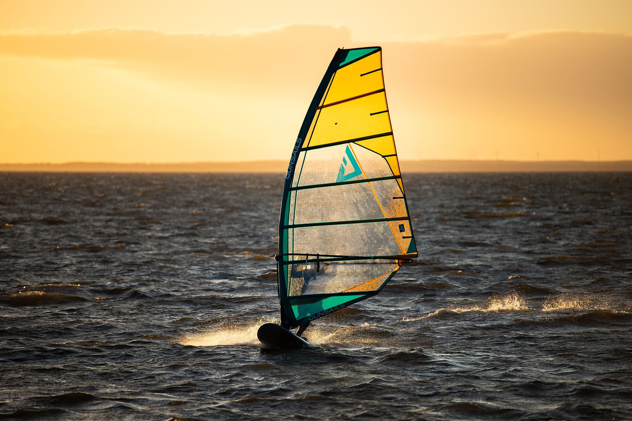 Une personne pratiquant la planche à voile sur une étendue d'eau au coucher du soleil.