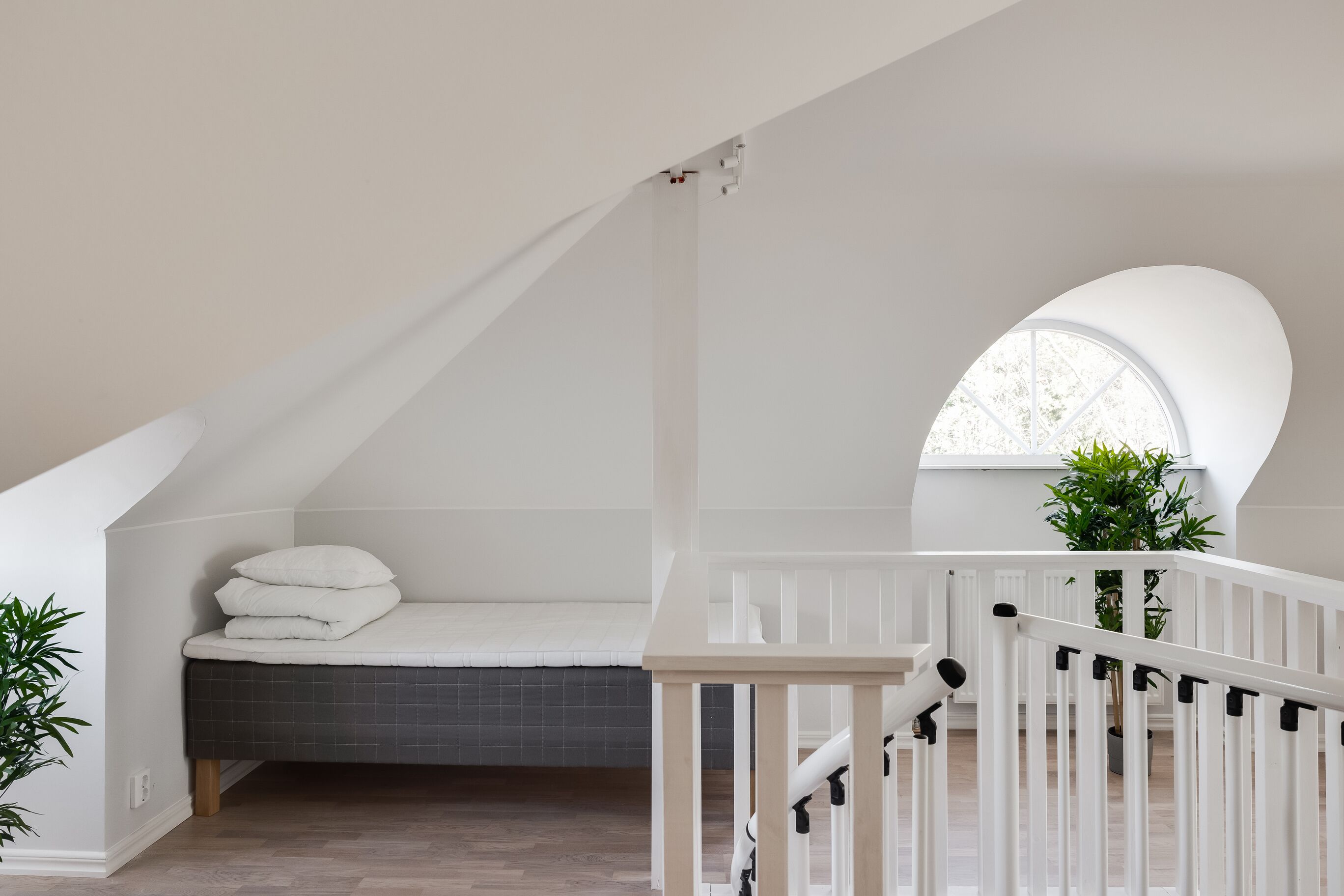 A bedroom with a sloped ceiling, a bed, a window, and a staircase.