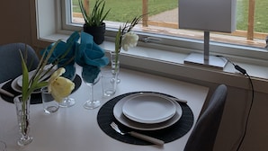 A dining table set with plates, cutlery, and a vase with flowers, overlooking a lakeside view with a wooden deck and picnic tables. - Stora Frögården (Morbylanga)
