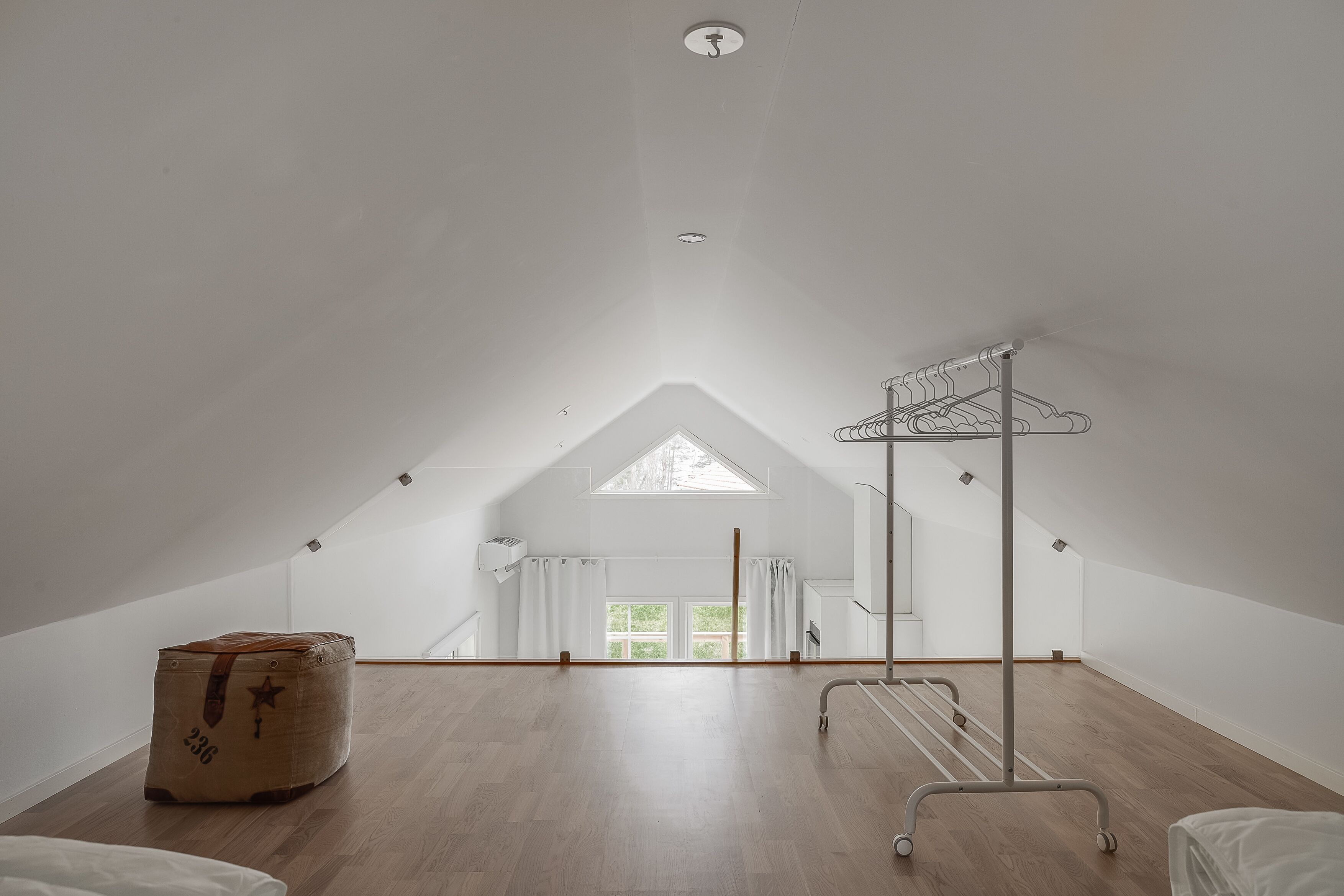 A spacious attic room with a sloped ceiling, a skylight, a wooden floor, a metal drying rack, and a large storage box.