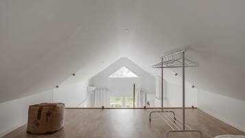 A spacious attic room with a sloped ceiling, a skylight, a wooden floor, a metal drying rack, and a large storage box.