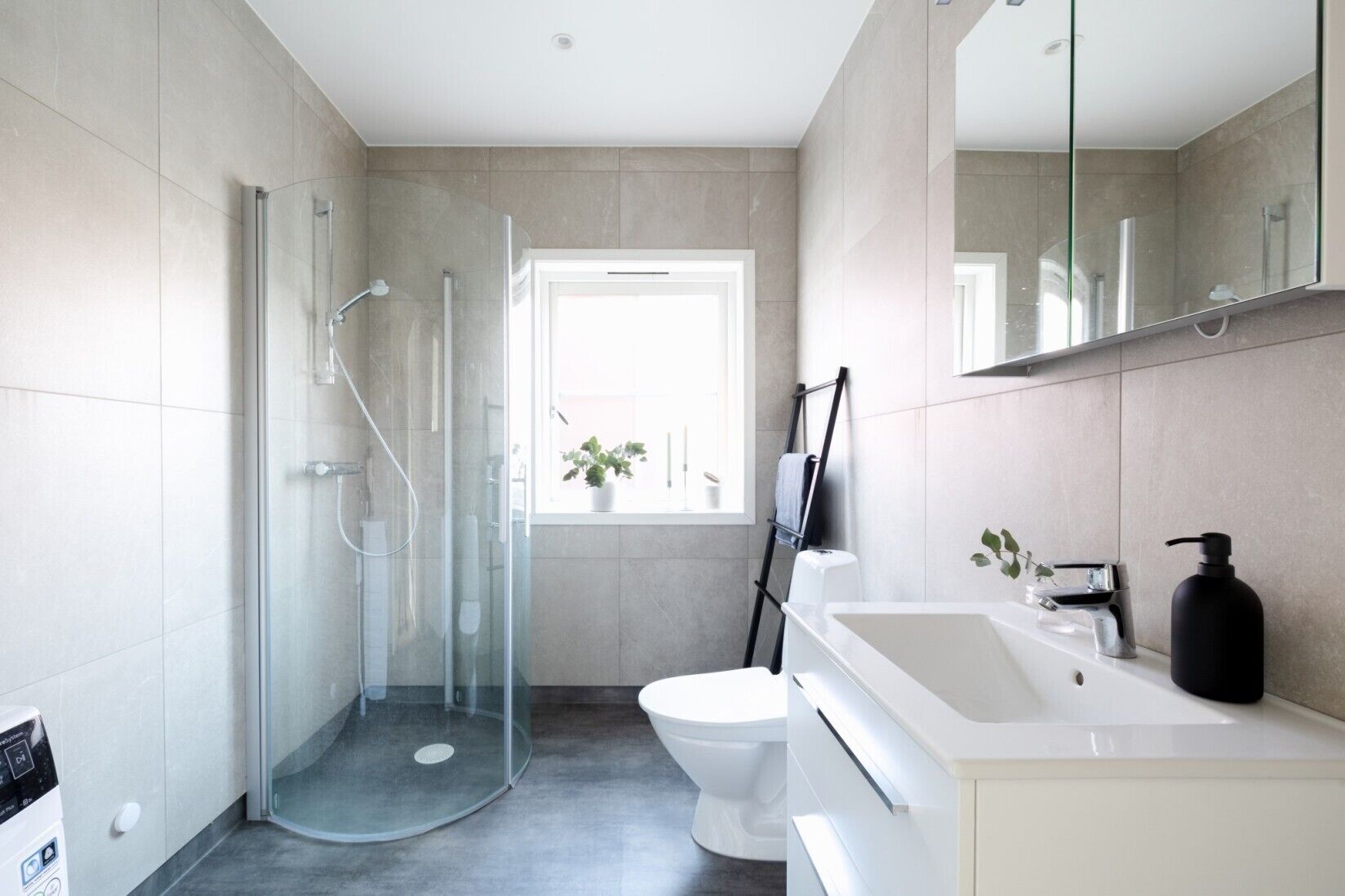 A modern bathroom with a glass shower enclosure, a toilet, a sink with a black soap dispenser, and a mirror above the sink.