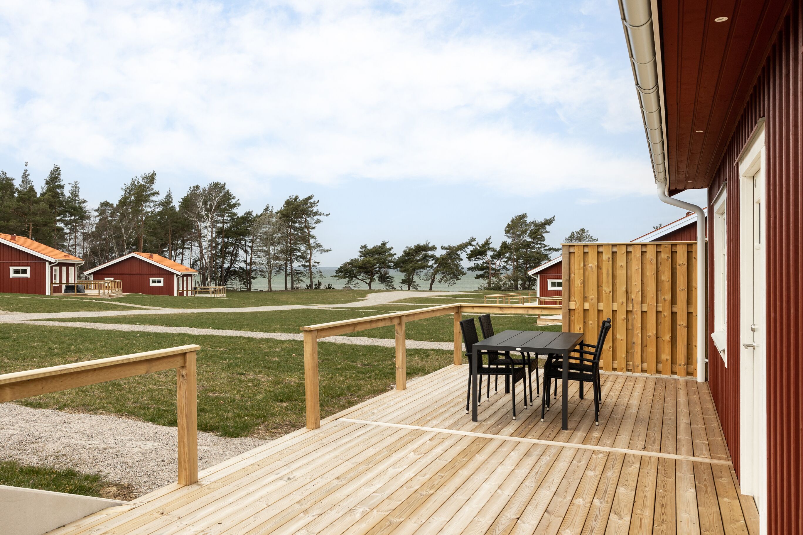 Una terraza de madera con una mesa y sillas, una valla de madera y vistas a edificios rojos y árboles.