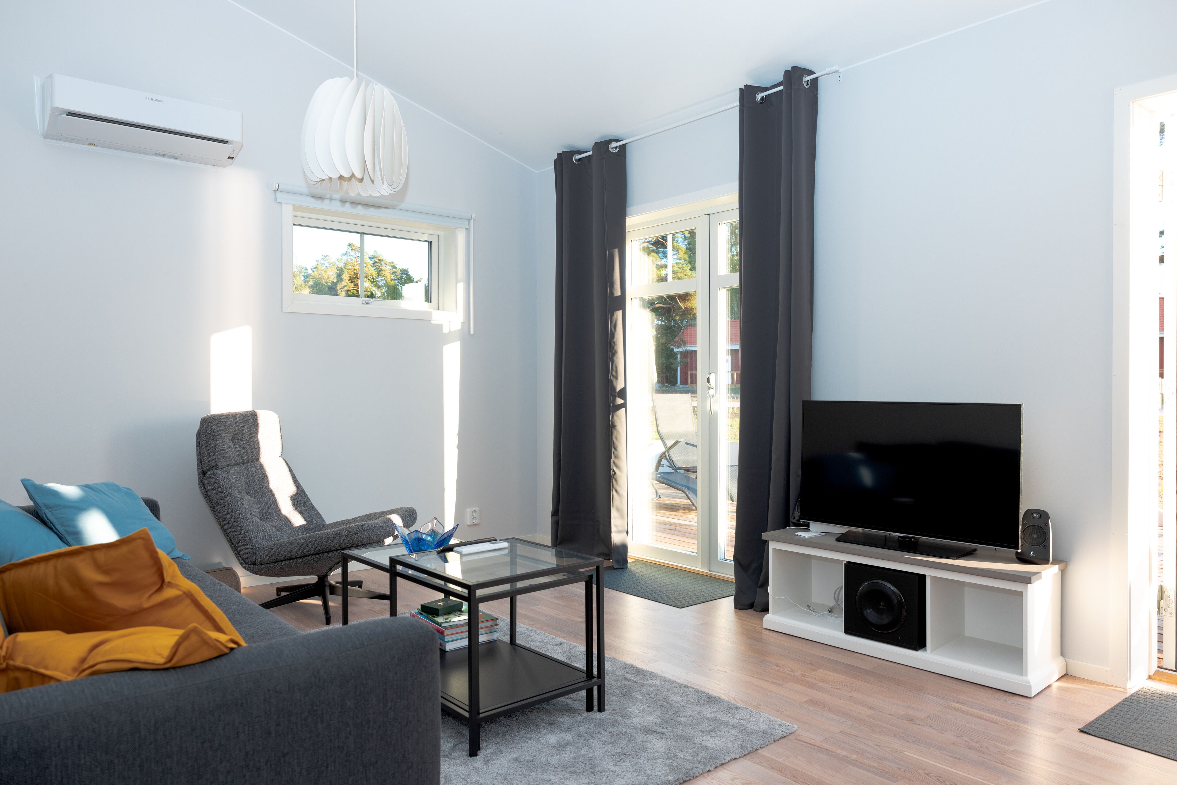 Ett modernt vardagsrum med en soffa, fåtölj, soffbord i glas, en platt-TV och en vit mediabänk.