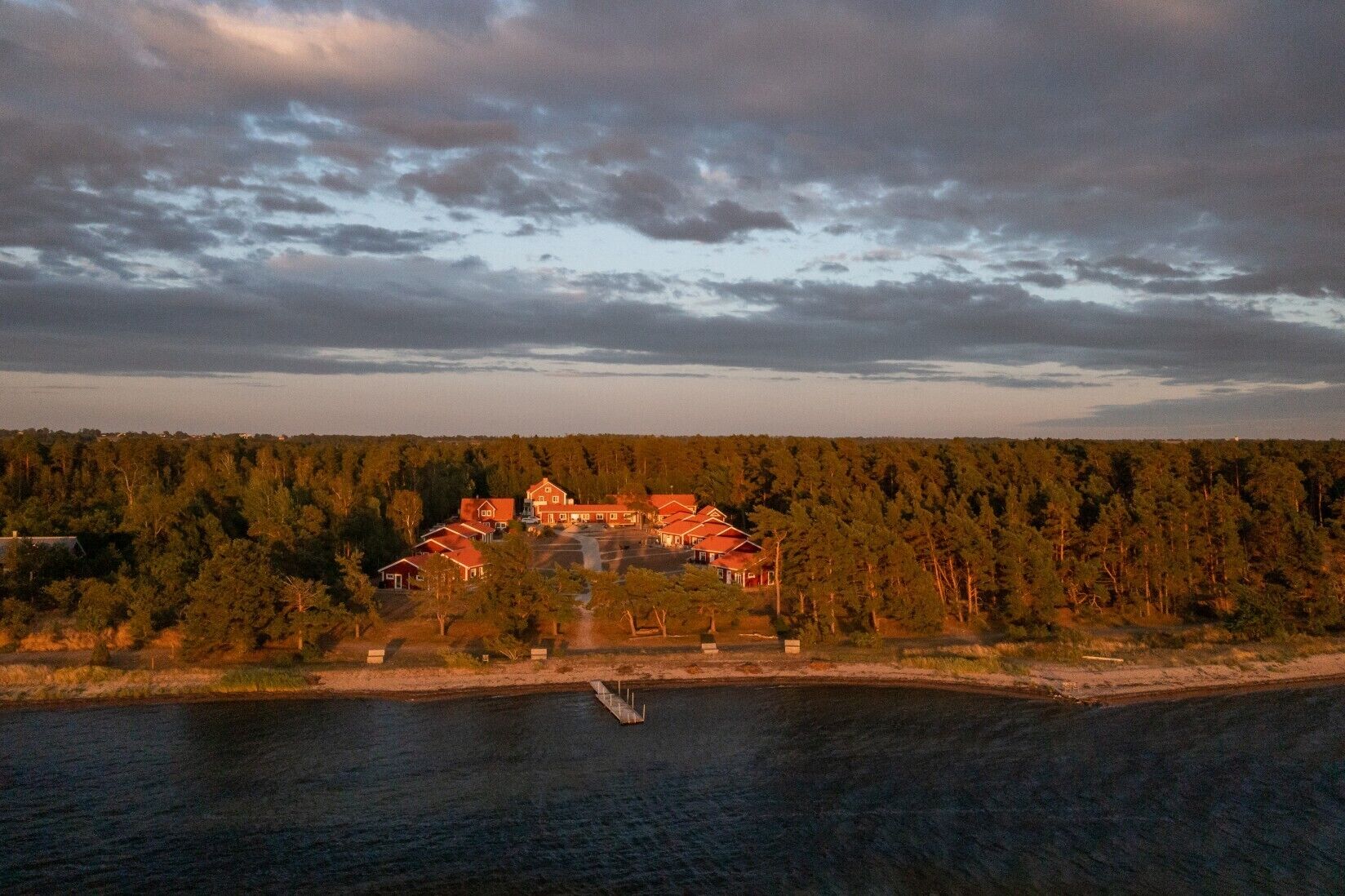 A lakeside property with a cluster of red-roofed buildings surrounded by dense forest.