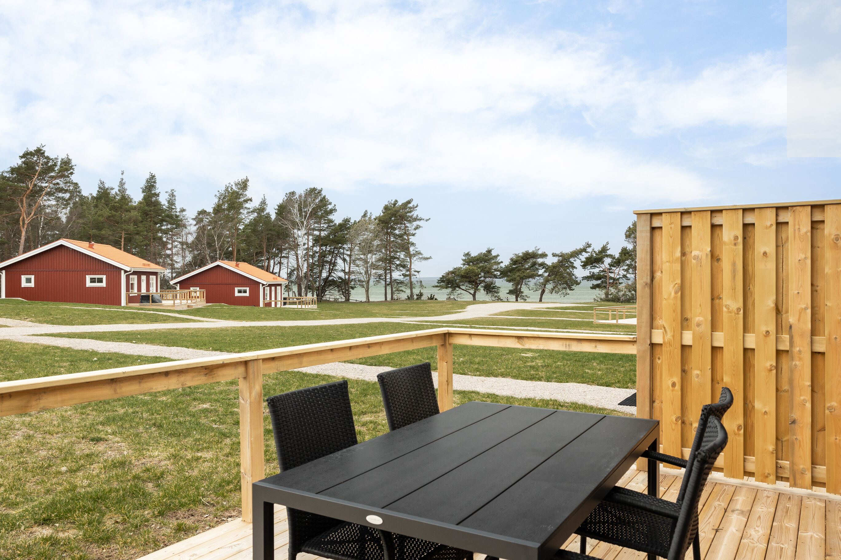 A wooden deck with a table and chairs, a wooden fence, and a red building in the background.