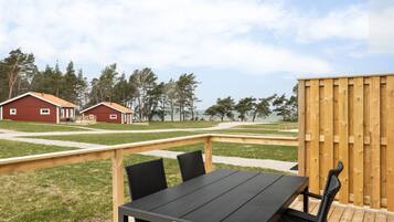 A wooden deck with a table and chairs, a wooden fence, and a red building in the background.
