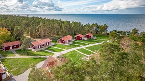 A coastal property with multiple red-roofed cabins arranged in a grid pattern, surrounded by a dense forest and a view of the sea. - Stora Frögården (Morbylanga)