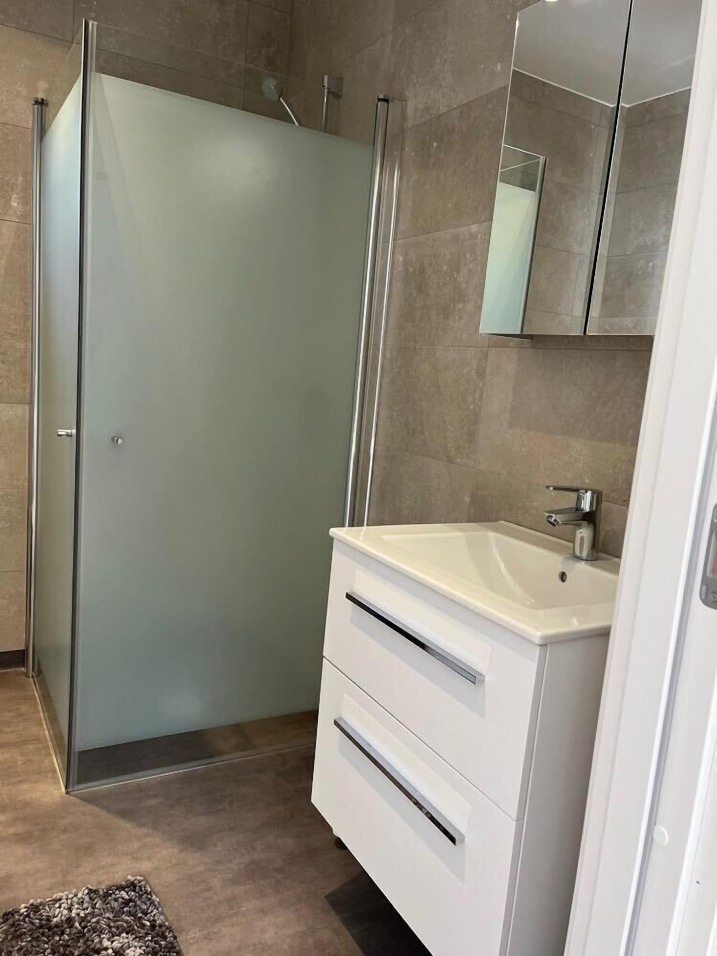 A modern bathroom with a glass shower enclosure, a white vanity with a sink, and a mirror above the vanity.