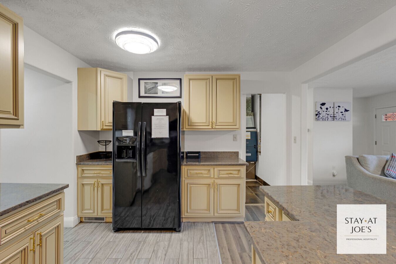 A modern kitchen with a black refrigerator, beige cabinets, and a granite countertop.