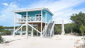 A two-story beach house with a balcony, a staircase, and a view of the ocean. - Blue Hole Lodge - Bonefish Heaven with Blue Hole in Backyard (Exuma)