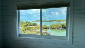 A room with a large window overlooking a coastal landscape with greenery and water. - Blue Hole Lodge - Bonefish Heaven with Blue Hole in Backyard (Exuma)