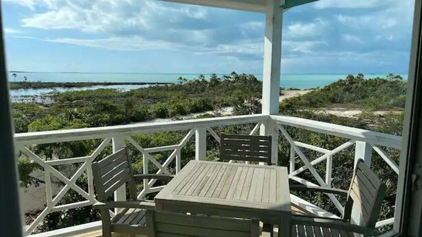 A covered outdoor area with a table and chairs, overlooking a beach and mangroves. - Blue Hole Lodge - Bonefish Heaven with Blue Hole in Backyard (Exuma)