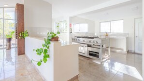 A modern kitchen with a stainless steel stove, white cabinetry, and large windows. - Valles apartamentos ecológicos (Urubamba)