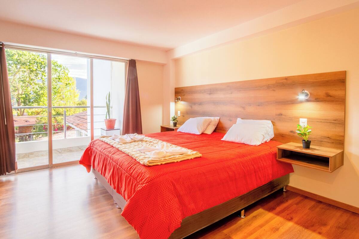 Ein Schlafzimmer mit einem großen Bett, einem Holzkopfende, einem Nachttisch, einer Topfpflanze und einer Glasschiebetür, die auf einen Balkon führt.
