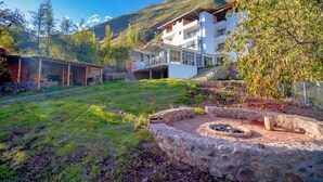 A modern two-story house with a stone fire pit in the yard, surrounded by a mountain backdrop. - Valles apartamentos ecológicos (Urubamba)