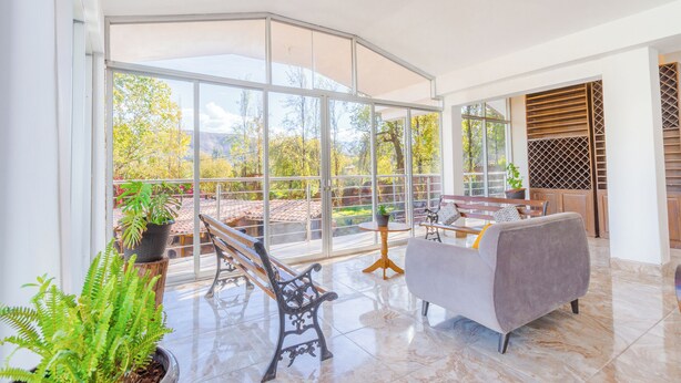 A spacious balcony with a view of trees and mountains, furnished with a sofa, a bench, and a table. - Valles apartamentos ecológicos (Urubamba)