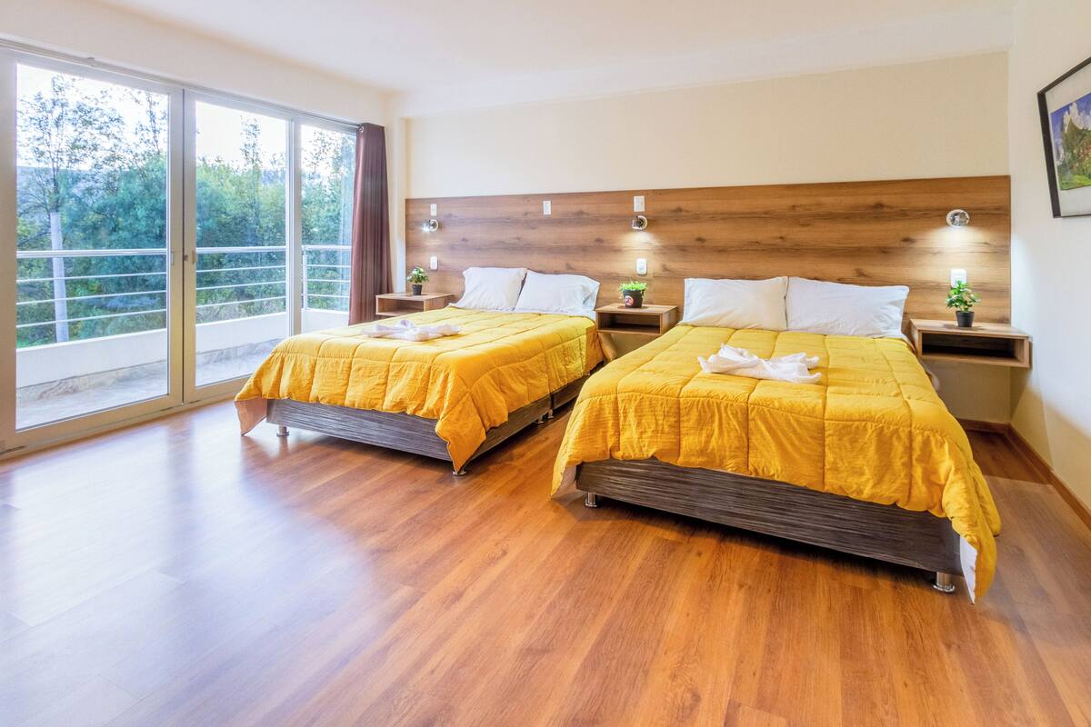 Ein Hotelzimmer mit zwei Betten, Holz-Kopfteilen, Nachttischen mit Lampen und einer großen Schiebeglastür, die auf einen Balkon führt.