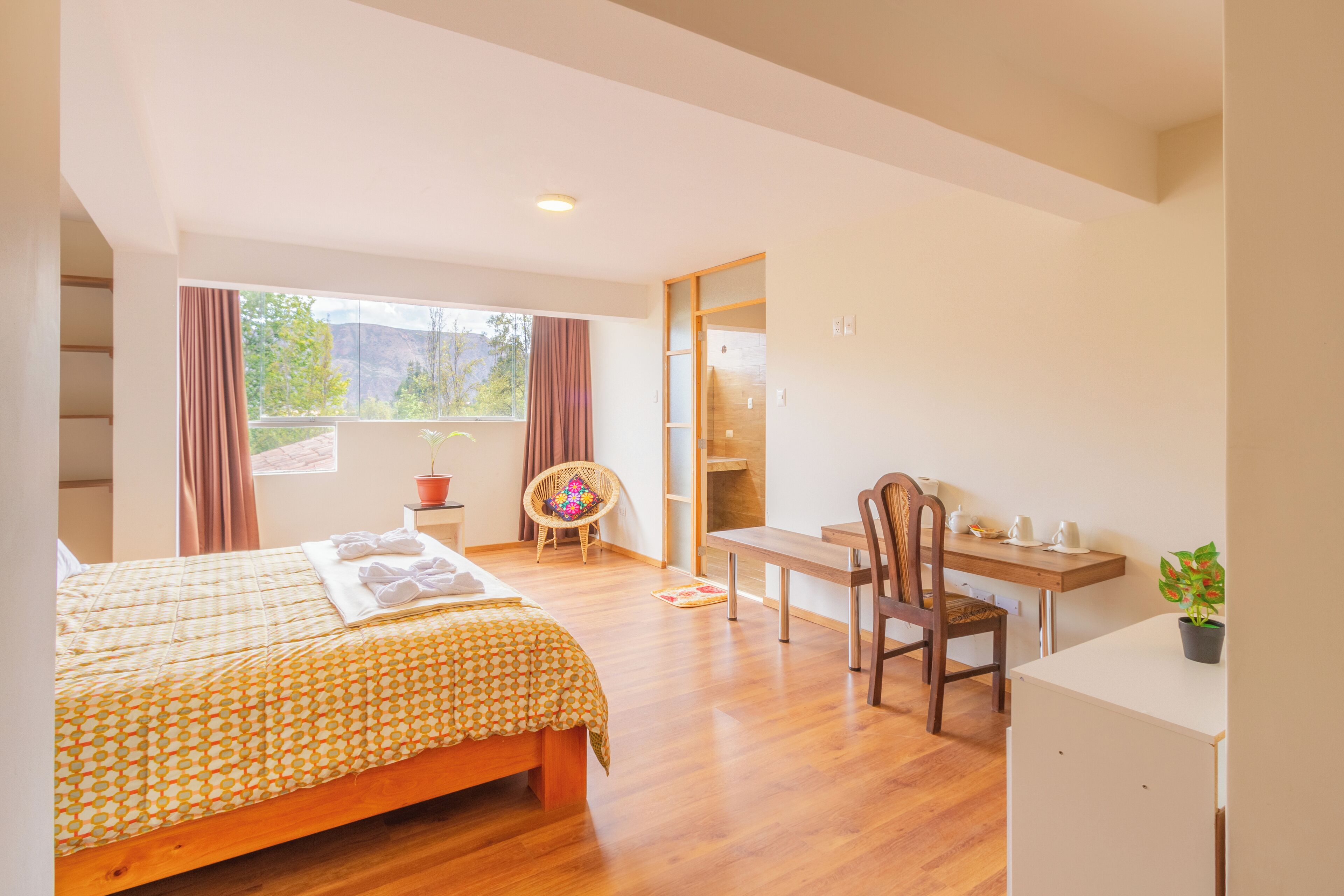 A bedroom with a bed, a desk, a chair, a potted plant, and a view of the outdoors.