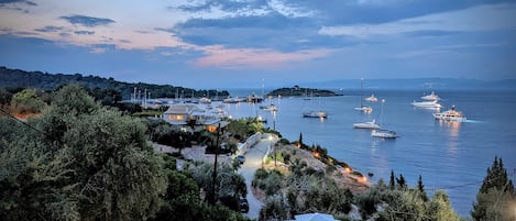Ein Küstenhafen mit vor Anker liegenden Booten, umgeben von Grünflächen und Hügeln.