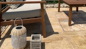Ein hölzerner Sitzbereich im Freien mit einer gepolsterten Bank und einem Tisch, einem Weidenlaternen und einem Steingärtchen.